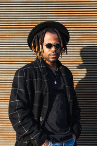 Portrait of young man wearing sunglasses standing against wall