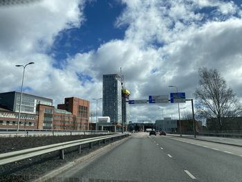 Road passing through city against cloudy sky