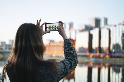 Rear view of young woman photographing against clear sky