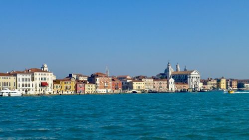 View of buildings by sea against blue sky