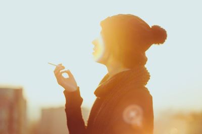 Close-up of young woman smoking cigarette against sky
