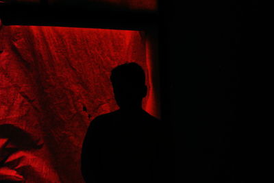 Silhouette man standing against red wall in darkroom