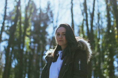 Portrait of young woman standing by tree in forest