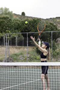 Vertical view of concentrated woman tennis player serving a tennis serve with the net