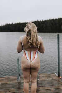 Rear view of woman sitting on pier over lake