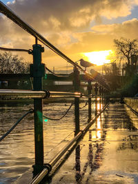 Wet bridge over river against sky during sunset