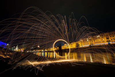 Light trails on river against sky at night