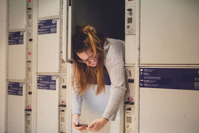 Young woman using phone in locker