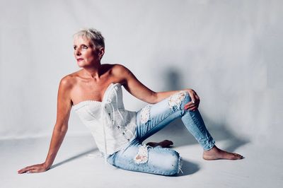 Thoughtful mature model wearing corset while sitting against white backdrop