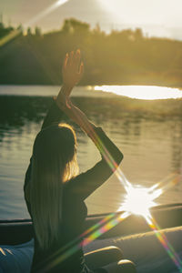 Rear view of woman with arms raised against sky during sunset