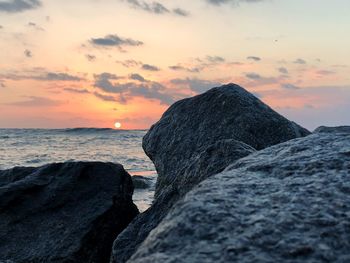 Rock on beach against sky during sunset