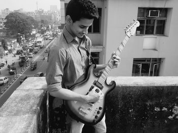 Young man playing guitar while standing on terrace