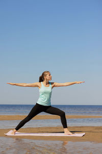 Full length of woman exercising at beach against clear sky