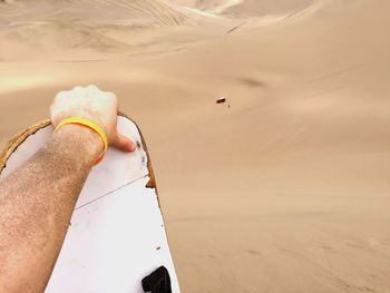 Cropped hand of man holding sandboard at desert