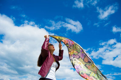 Low angle view of woman holding fabric against sky