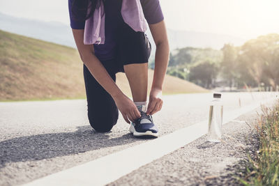 Low section of athlete tying shoelace while crouching on road 