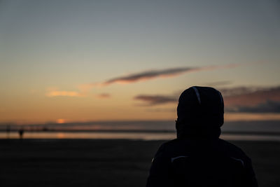 Rear view of silhouette man on beach against sky during sunset