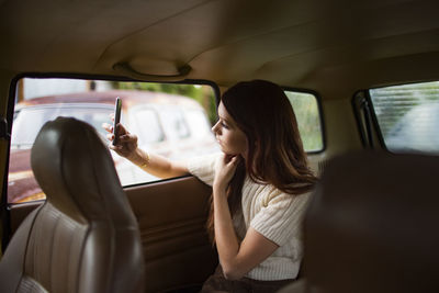 Teenager photographing through smart phone while sitting in car