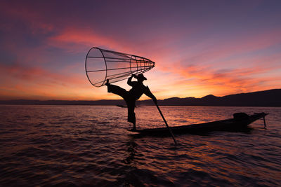 Silhouette man fishing net on lake at sunset