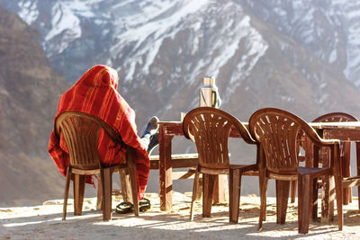 Rear view of man sitting on chair against snowcapped mountain