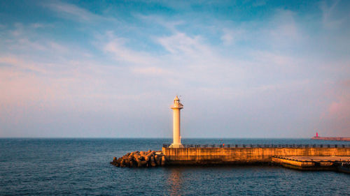 Lighthouse by sea and buildings against sky