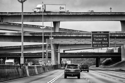 Road sign on bridge against sky in city