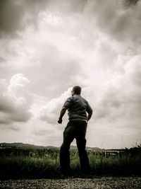 Rear view of man standing on field against storm clouds