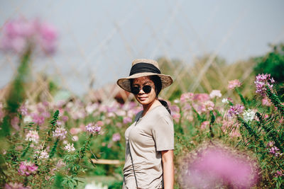 Portrait of woman wearing sunglasses while standing by flowering plants
