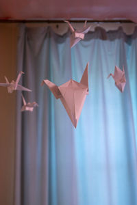 Pastel pink paper cranes suspended on strings or strings in close-up on a blurry background of blue 