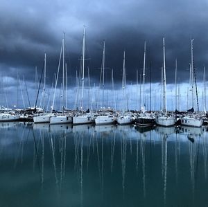 Sailboats moored in sea against cloudy sky