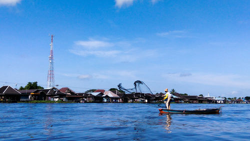 Side view of mid adult man standing in boat on sea against blue sky