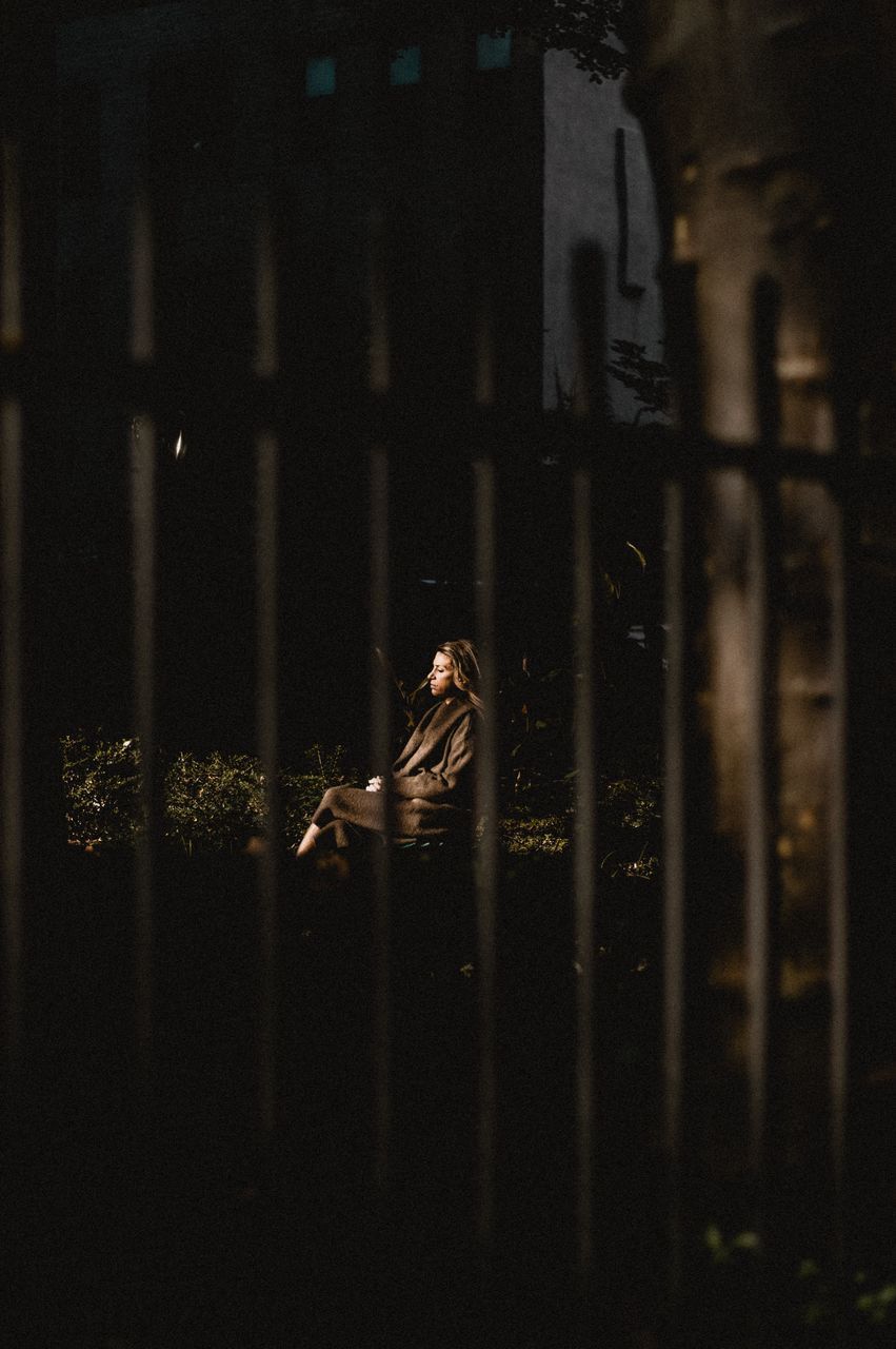 SIDE VIEW OF WOMAN SITTING ON WINDOW