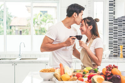 Boyfriend kissing girlfriend while standing by food in kitchen