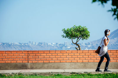 Rear view of woman standing by wall against clear sky