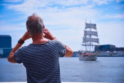 Rear view of man standing in harbor against sky