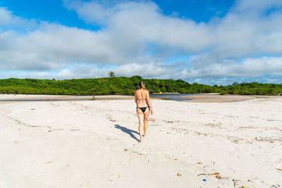 Rear view of woman walking at beach against sky