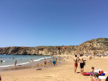 People on beach against clear blue sky