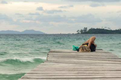 Woman sitting on pier over sea against sky