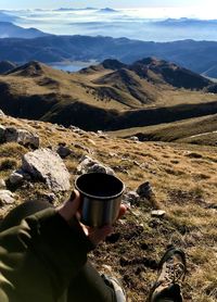 Cropped hand of woman holding coffee cup against landscape