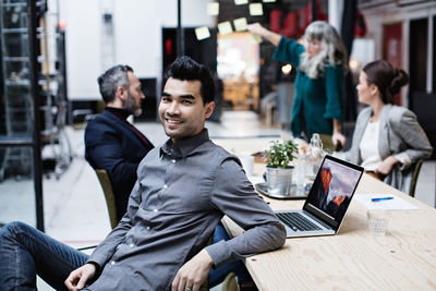 Portrait of smiling businessman sitting with colleagues in meeting at office