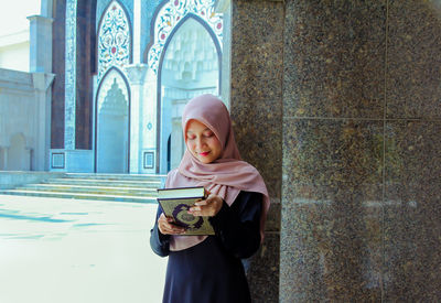 Woman holding holy book while standing against architectural column