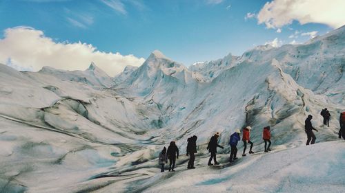 Hikers walking on snowcapped mountains against sky