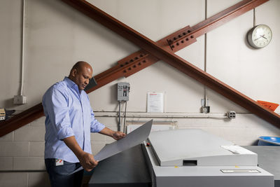 Supervisor examining paper while standing by print machine in shop