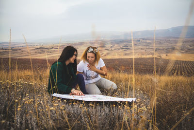 Young woman discussing map with friend on field against sky