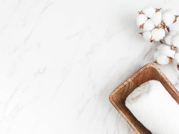 Cotton towels on wood tray and cotton branch on white marble background.