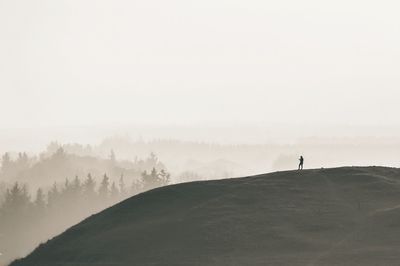 Mid distance of person standing on landscape against sky during foggy weather