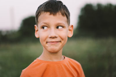 Portrait of a smiling little boy in a orange t-shirt and playing outdoors on the field at sunset