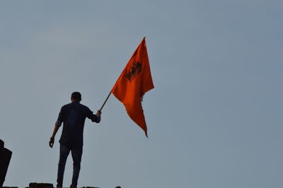 Rear view of man holding red flag against clear sky