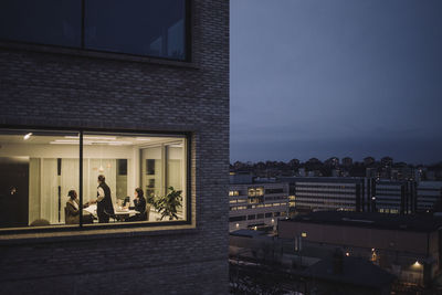 Multiracial female colleagues working late seen through window of work place