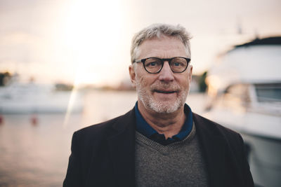 Portrait of senior man smiling at harbor during sunset